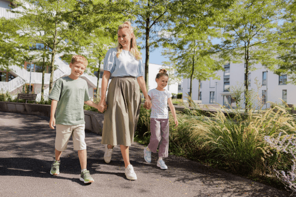 Eine Mutter geht mit zwei Kindern auf einem sonnigen Parkweg spazieren.