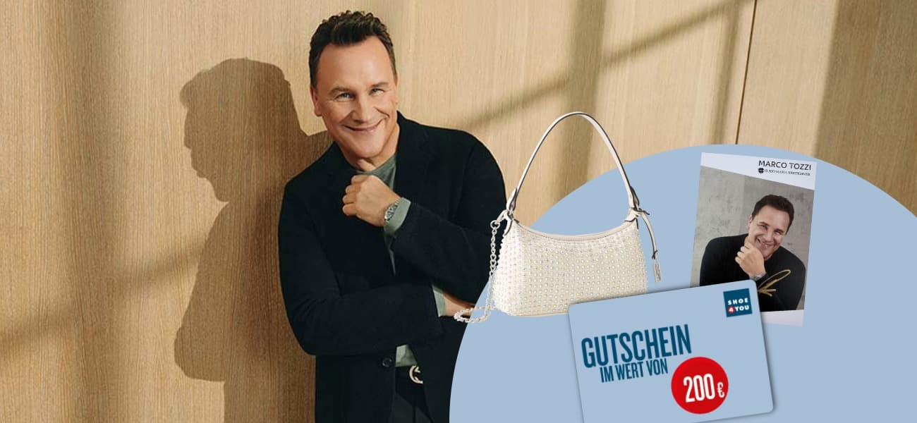 Man in black jacket leaning against a wooden wall, with a white handbag and a 200€ gift card on a blue circle.