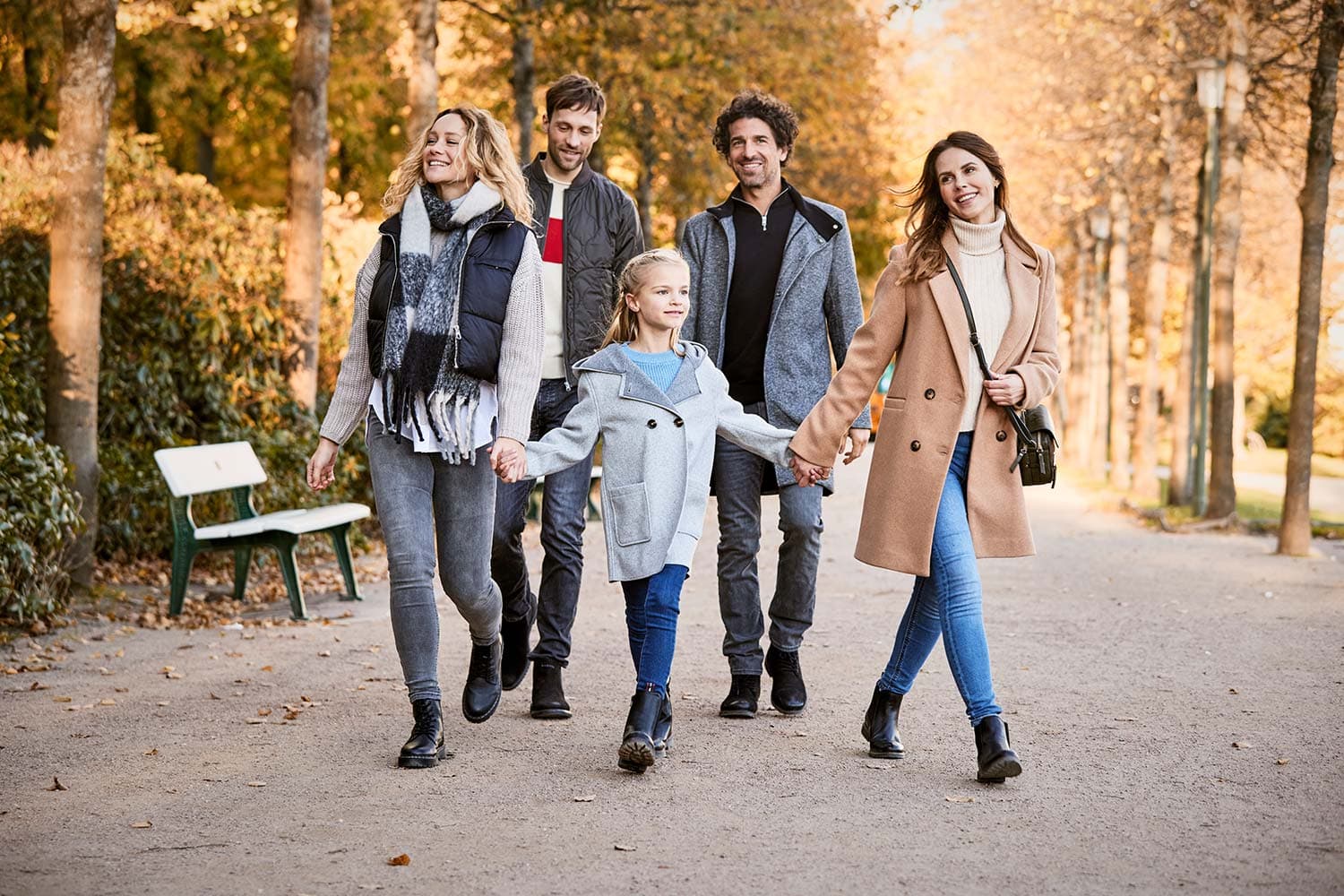 Eine Familie bei einem Herbst-Spaziergang durch den Park in herbstlicher Kleidung mit Schal und Stiefeln