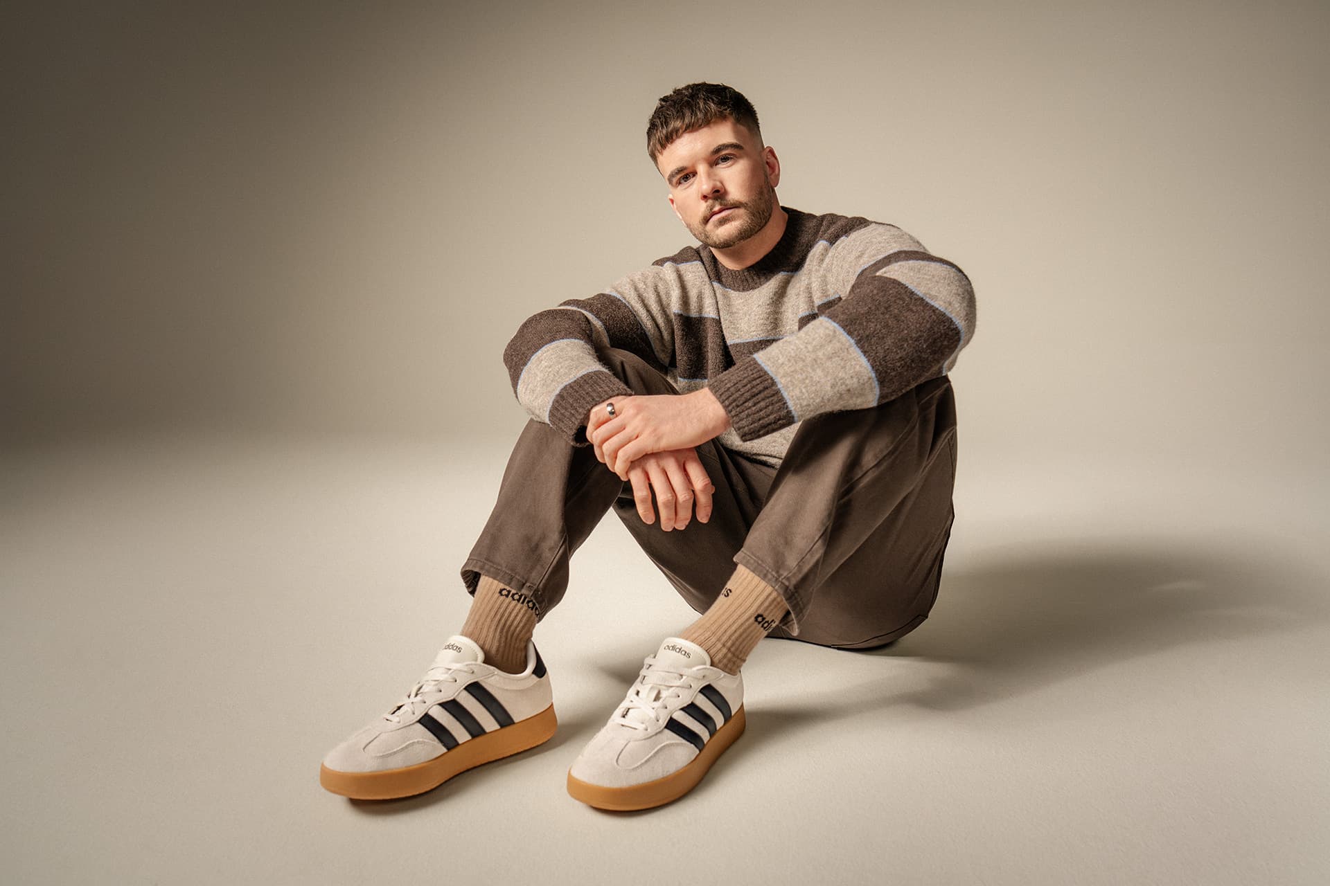 Person in Freizeitkleidung, mit gestreiftem Pullover und brauner Hose. Neutraler Hintergrund.